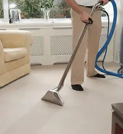 Professional carpet cleaner using a hot-water extraction wand and hose machine in a living room in Tulsa, OK.