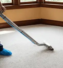 Steam carpet cleaning technician using a hot-water extraction wand on a residential carpet, wearing blue protective shoe covers Tulsa, OK.