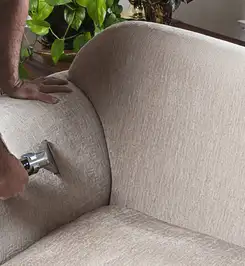 Professional upholstery cleaner deep-cleaning a fabric sofa with a handheld extraction tool and hose Tulsa, OK.